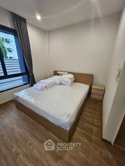 Modern bedroom with large window and wooden flooring in a stylish apartment.