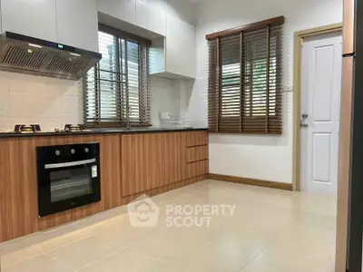 Modern kitchen with sleek wooden cabinets and built-in oven, featuring gas stove and ample natural light.
