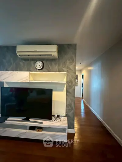 Modern living room with TV and air conditioning, featuring stylish wall design and wooden flooring.