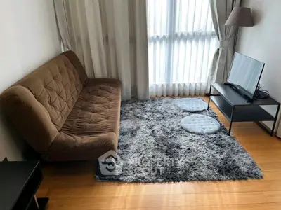 Cozy living room with brown sofa, plush rug, and modern TV setup in bright apartment.