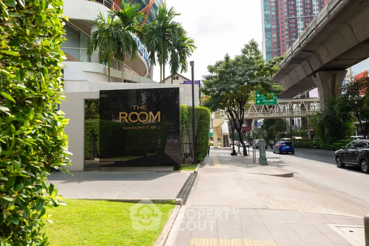 Modern urban building entrance with lush greenery and city street view, ideal for upscale living.