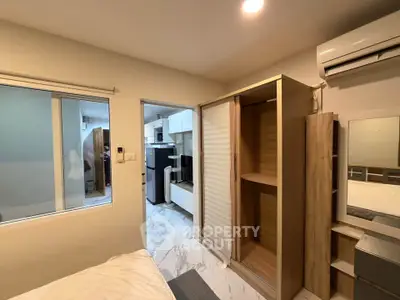 Modern bedroom with built-in wardrobe and air conditioning, adjacent to a sleek kitchen area.