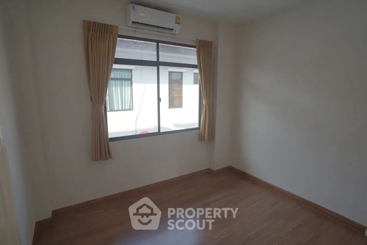 Spacious empty room with wooden flooring and large window, perfect for customization.