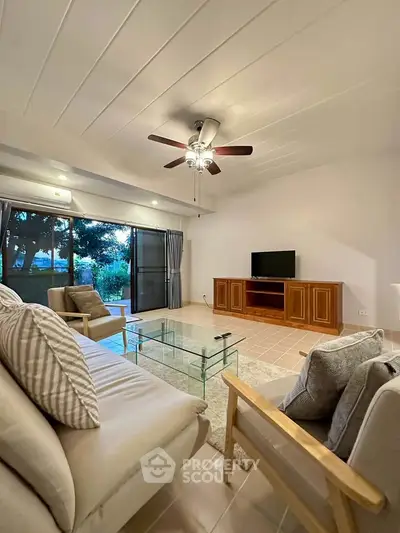 Spacious living room with modern decor and garden view, featuring a ceiling fan and glass coffee table.