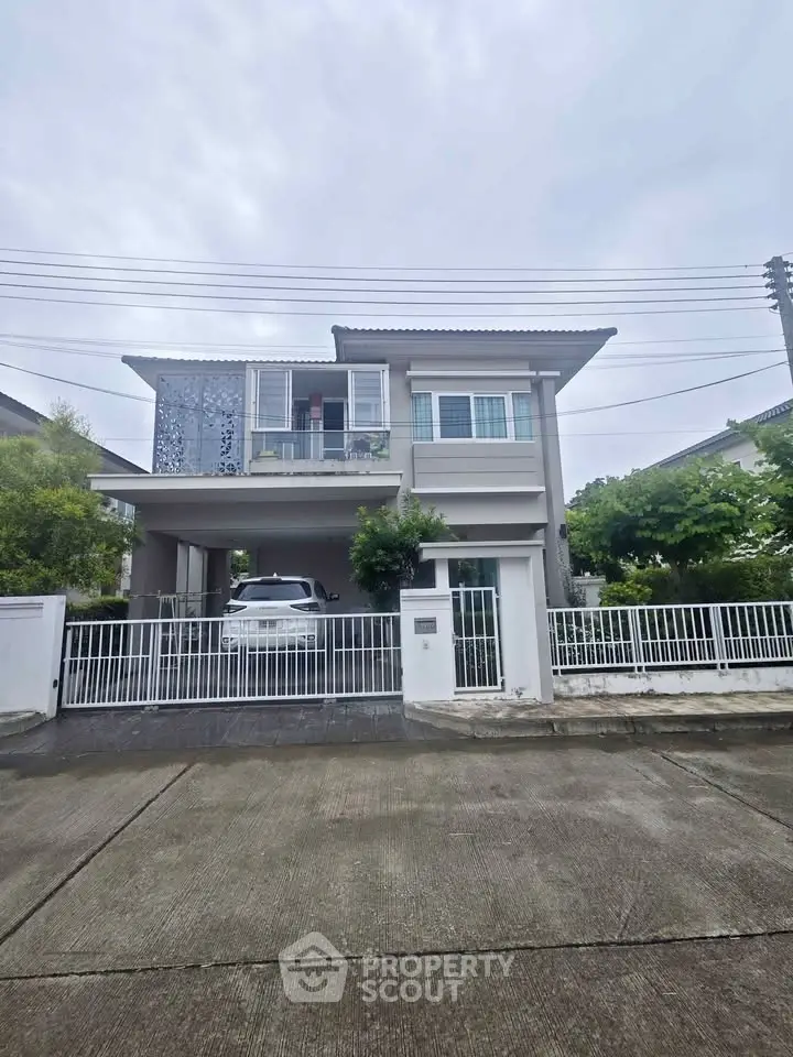 Modern two-story house with carport and lush greenery in a serene neighborhood.