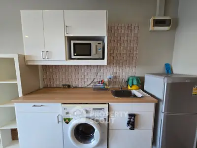Modern kitchen with washing machine, microwave, and fridge in compact layout.