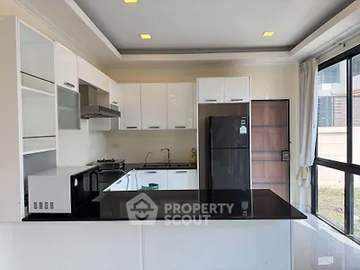 Modern kitchen with sleek white cabinets and black countertops, featuring a fridge and microwave.