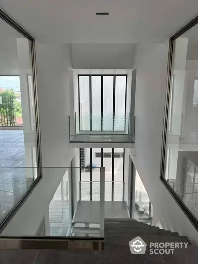 Modern minimalist staircase with glass railings and large windows offering natural light.