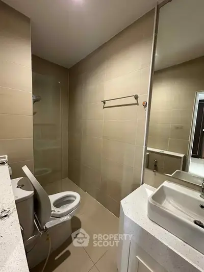 Modern bathroom with sleek fixtures and neutral tones, featuring a toilet and shower area.