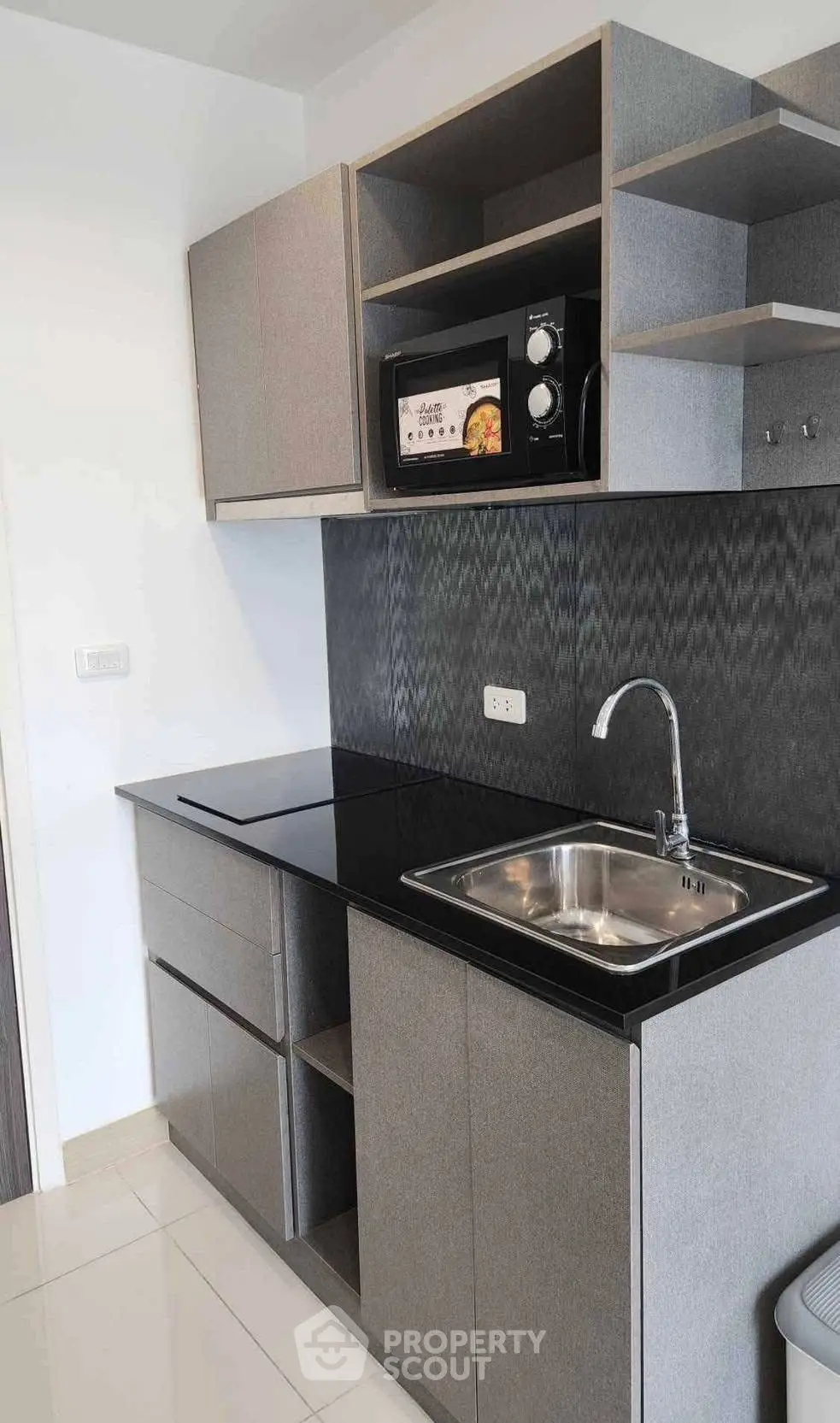 Modern kitchen with sleek cabinetry and built-in microwave, featuring a stylish black countertop and stainless steel sink.
