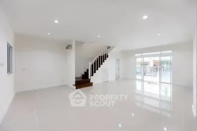 Spacious modern living room with glossy tile flooring and staircase, featuring large windows for natural light.