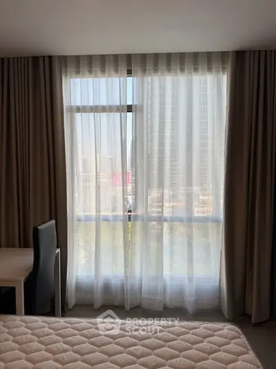 Cozy bedroom with large window and elegant curtains offering natural light and city view.
