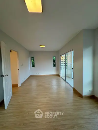 Spacious empty room with wooden flooring and large windows for natural light.