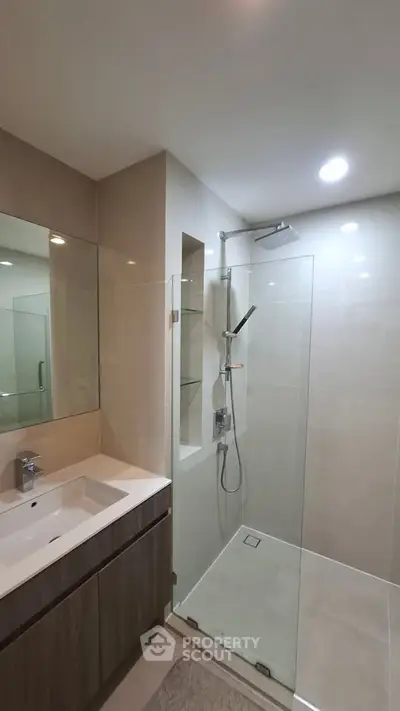 Modern bathroom with glass shower enclosure and sleek vanity in contemporary apartment.