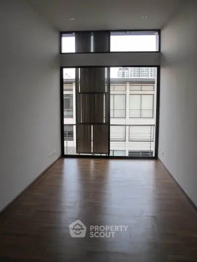 Spacious room with large windows and wooden flooring, ideal for modern living.