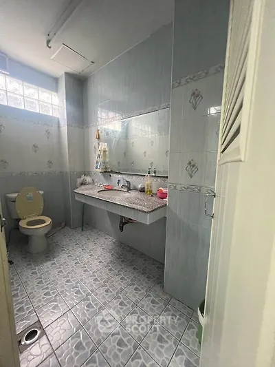 Spacious bathroom with tiled walls and floor, featuring a large mirror and modern fixtures.