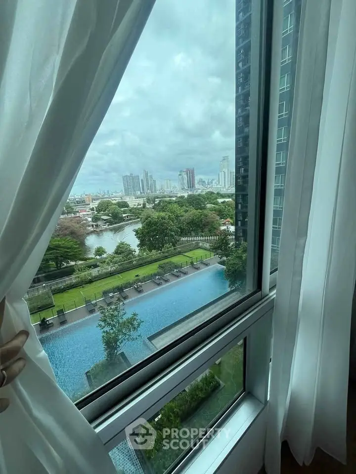 Stunning cityscape view from high-rise window overlooking pool and lush greenery.