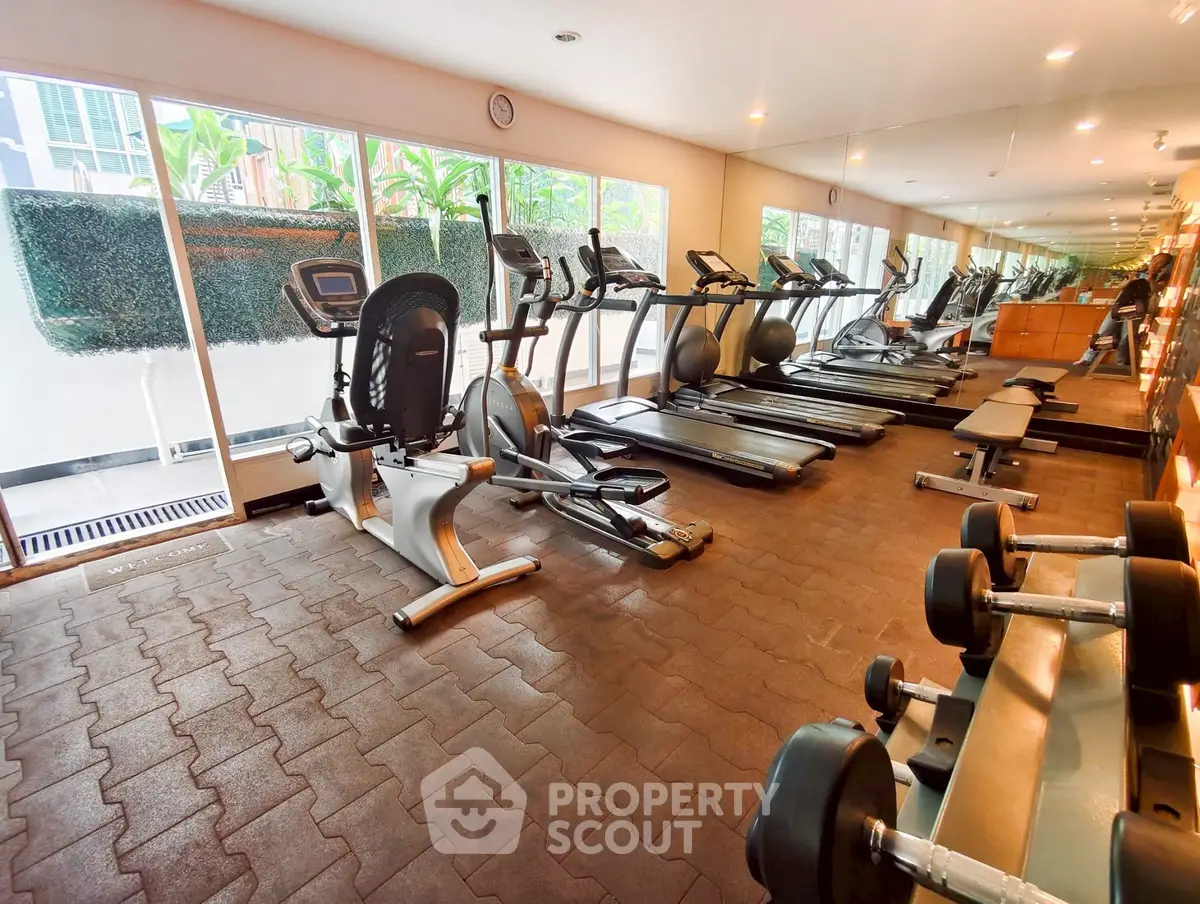 Spacious gym with modern equipment and large mirrors in luxury apartment complex.