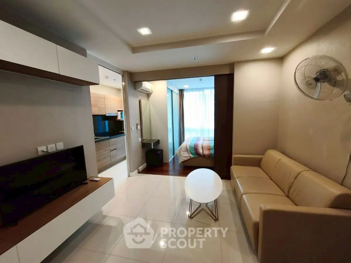 Modern living room with open layout to kitchen and bedroom, featuring sleek furniture and bright lighting.