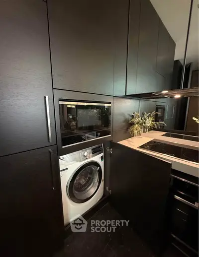 Modern kitchen with sleek black cabinetry and built-in appliances, featuring a washing machine and electric stove.