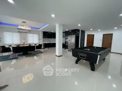 Spacious modern living area with pool table and dining space, featuring sleek kitchen design.
