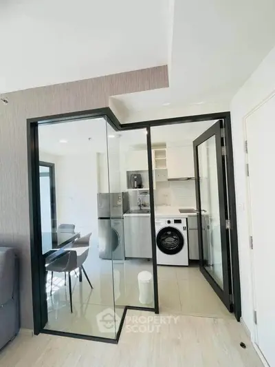 Modern kitchen with glass doors, washing machine, and sleek dining area in a stylish apartment.