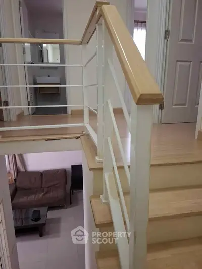 Modern interior staircase with wooden handrails and a view of a cozy living room below.