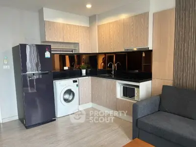 Modern kitchen with sleek appliances and cozy living area in open layout apartment.