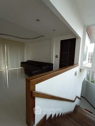 Modern living room with sleek staircase and large windows, offering ample natural light and contemporary design.