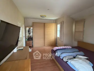 Spacious bedroom with wooden flooring and large wardrobe, featuring a cozy bed and modern TV setup.