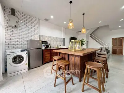 Modern kitchen with island, washing machine, and stylish lighting in open layout.