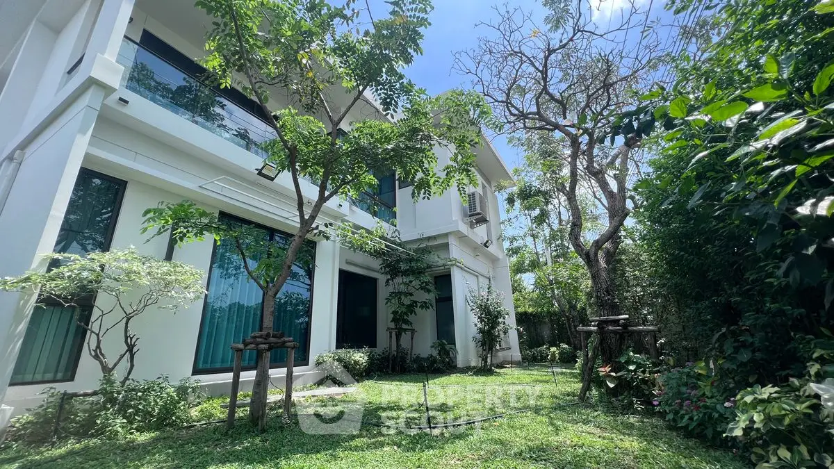 Modern two-story house with lush garden and large windows in a serene setting.