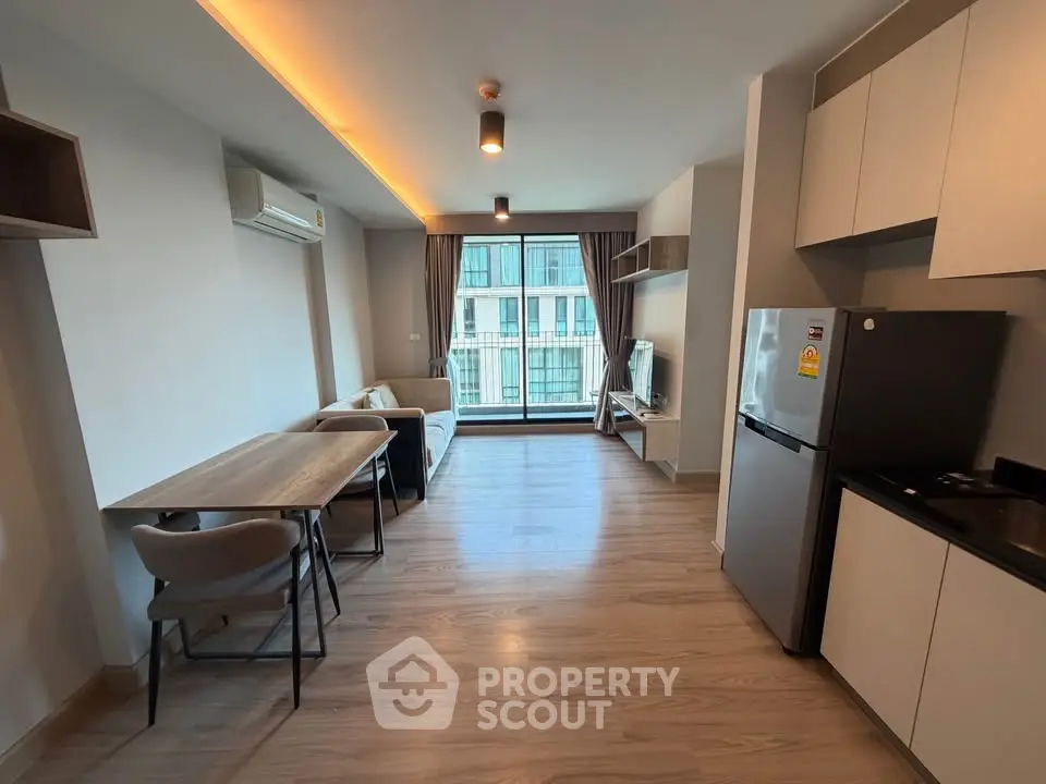 Modern open-layout living room with kitchen, featuring sleek furniture and large window view.