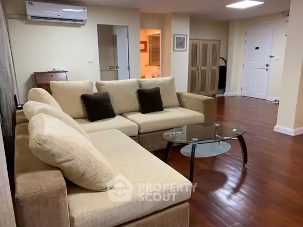 Spacious living room with modern beige sofa and glass coffee table on wooden flooring.