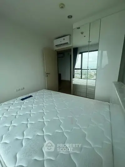 Modern bedroom with large window and mirrored wardrobe offering city views.