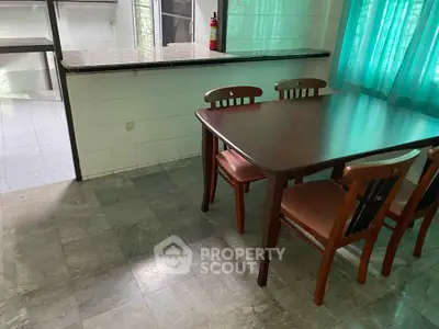 Spacious dining area with wooden table and chairs, adjacent to a tiled kitchen with open layout.