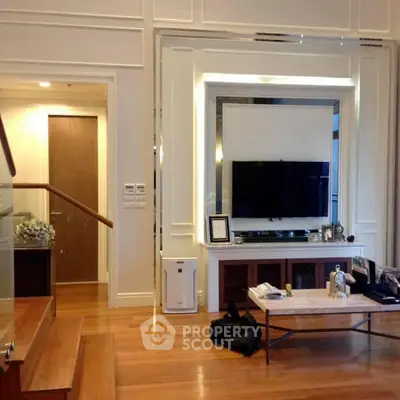 Elegant living room with modern decor and wooden flooring, featuring a large TV and stylish furniture.