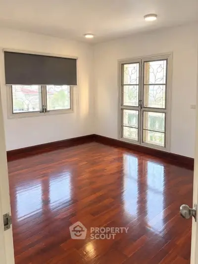 Spacious empty room with polished wooden floors and large windows, perfect for customization.
