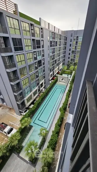 Modern apartment complex with a central swimming pool and lush greenery.