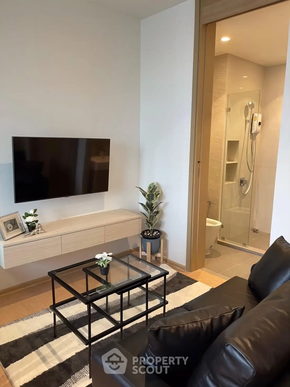 Modern living room with sleek black leather sofa, wall-mounted TV, and glass coffee table, adjacent to a stylish bathroom.