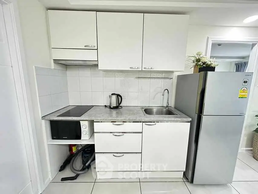 Modern compact kitchen with sleek white cabinets and stainless steel appliances.