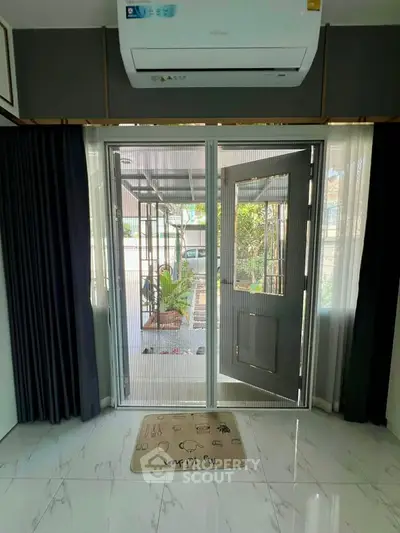 Modern living room with glass doors leading to a garden, featuring sleek air conditioning and elegant curtains.