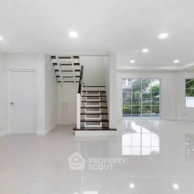 Spacious modern living room with sleek staircase and large windows offering natural light.