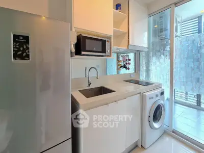 Modern compact kitchen with washing machine and sleek appliances in a bright apartment.