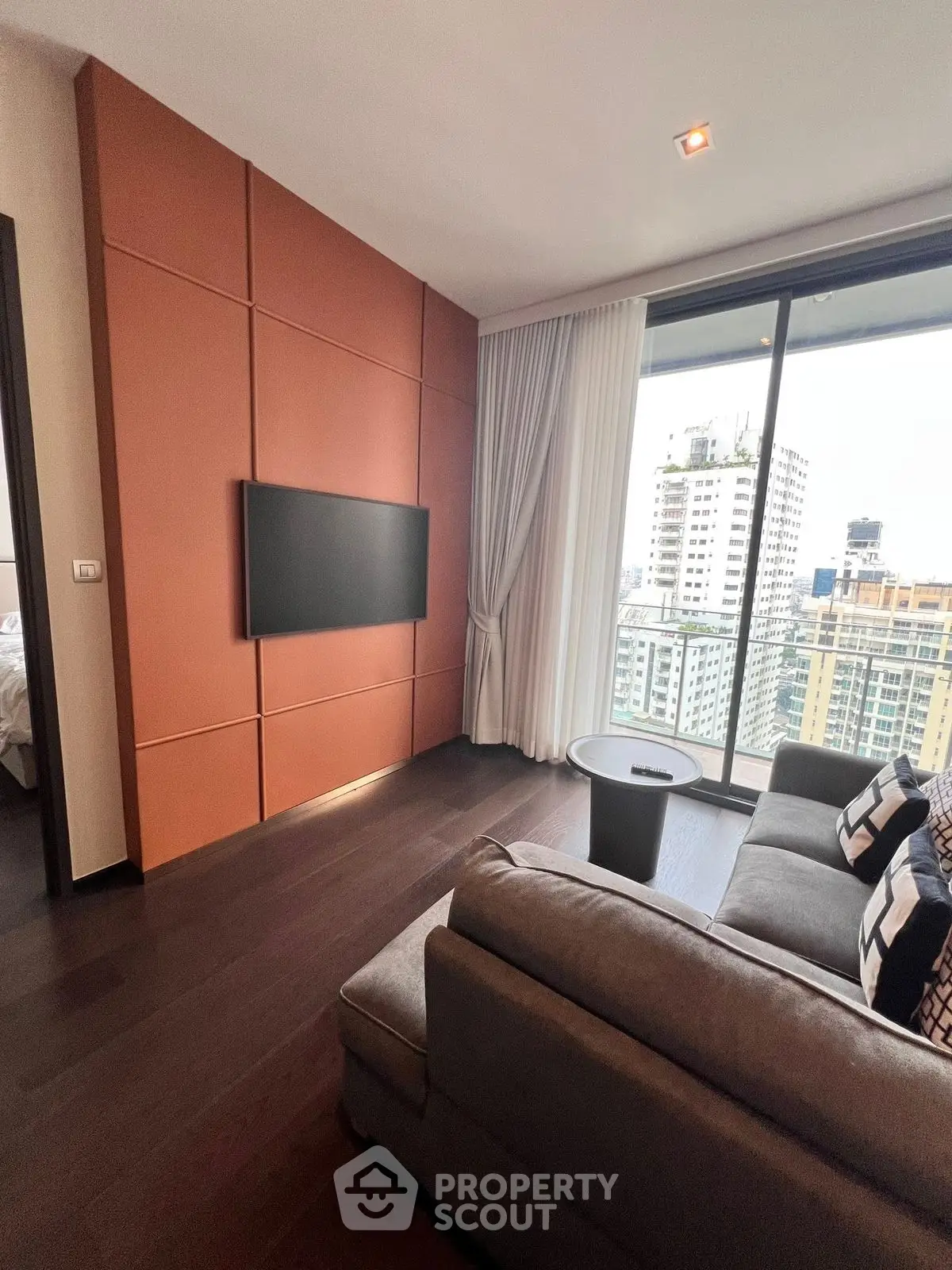 Modern living room with city view, stylish sofa, and wall-mounted TV in a high-rise apartment.