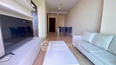 Modern living room with sleek furniture and open layout, featuring a large TV and dining area.