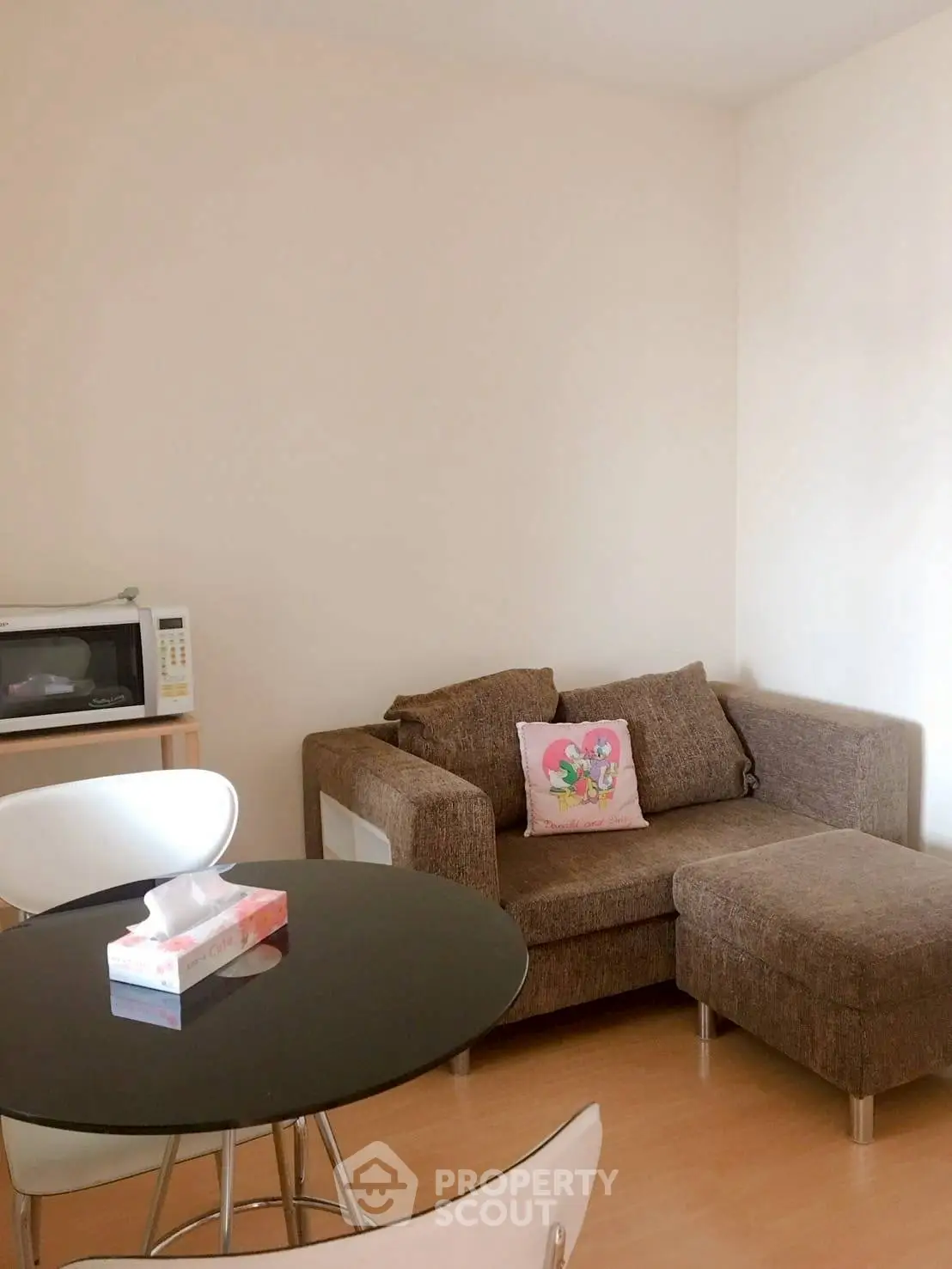 Cozy living room with brown sofa and dining table, featuring a microwave and bright decor.