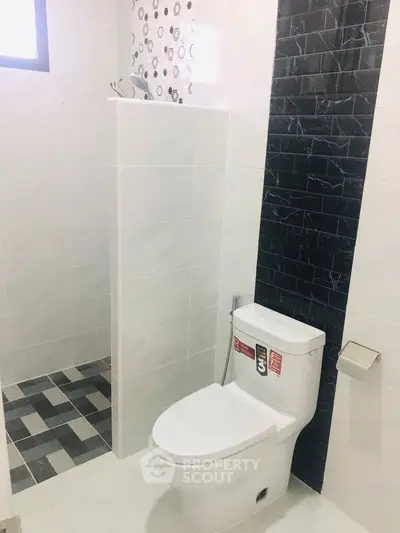 Modern bathroom with sleek design and stylish tile accents, featuring a contemporary toilet and shower area.