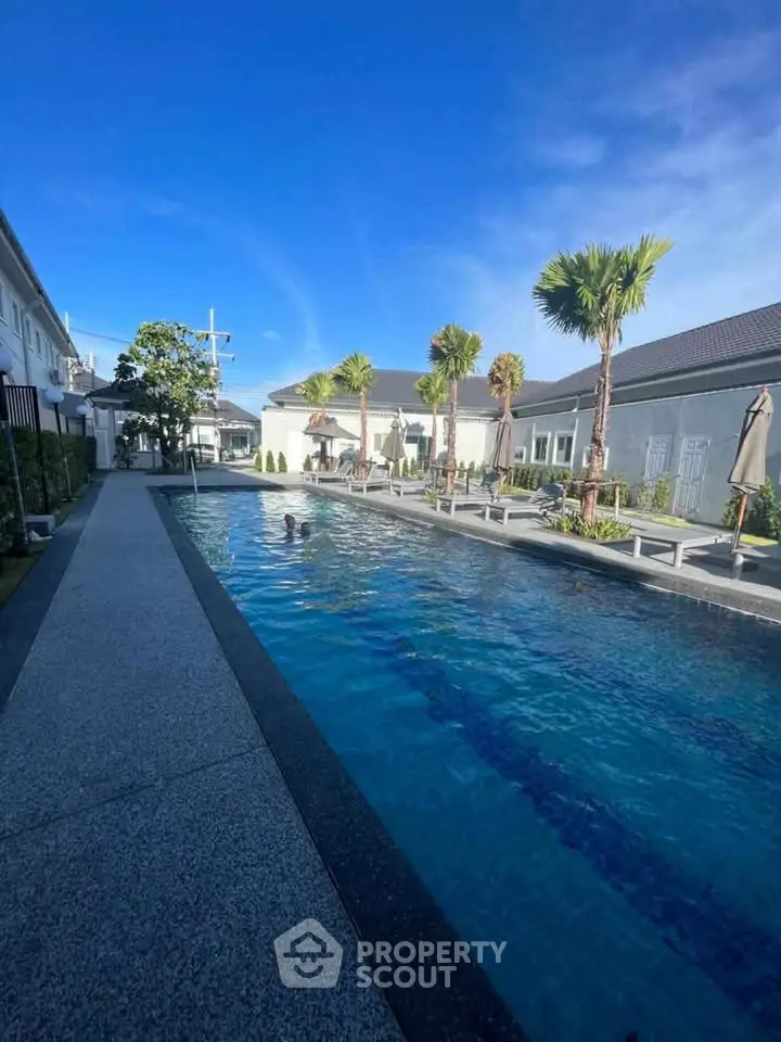 Luxurious residential pool area with palm trees and sun loungers under a clear blue sky.