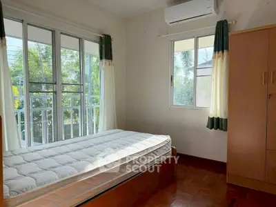 Bright bedroom with large windows and air conditioning, featuring a single bed and wardrobe.